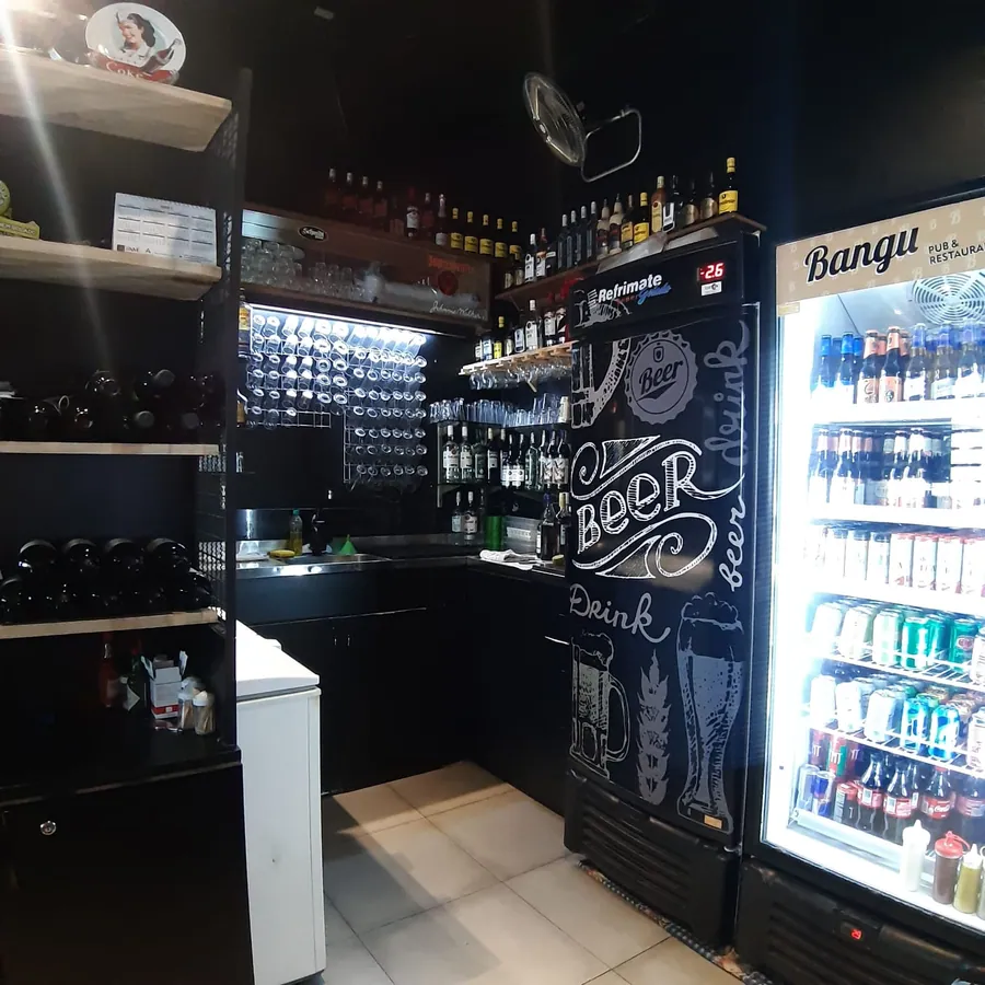 Balcão do pub Bangu com prateleiras de bebidas e copos sob luz acolhedora