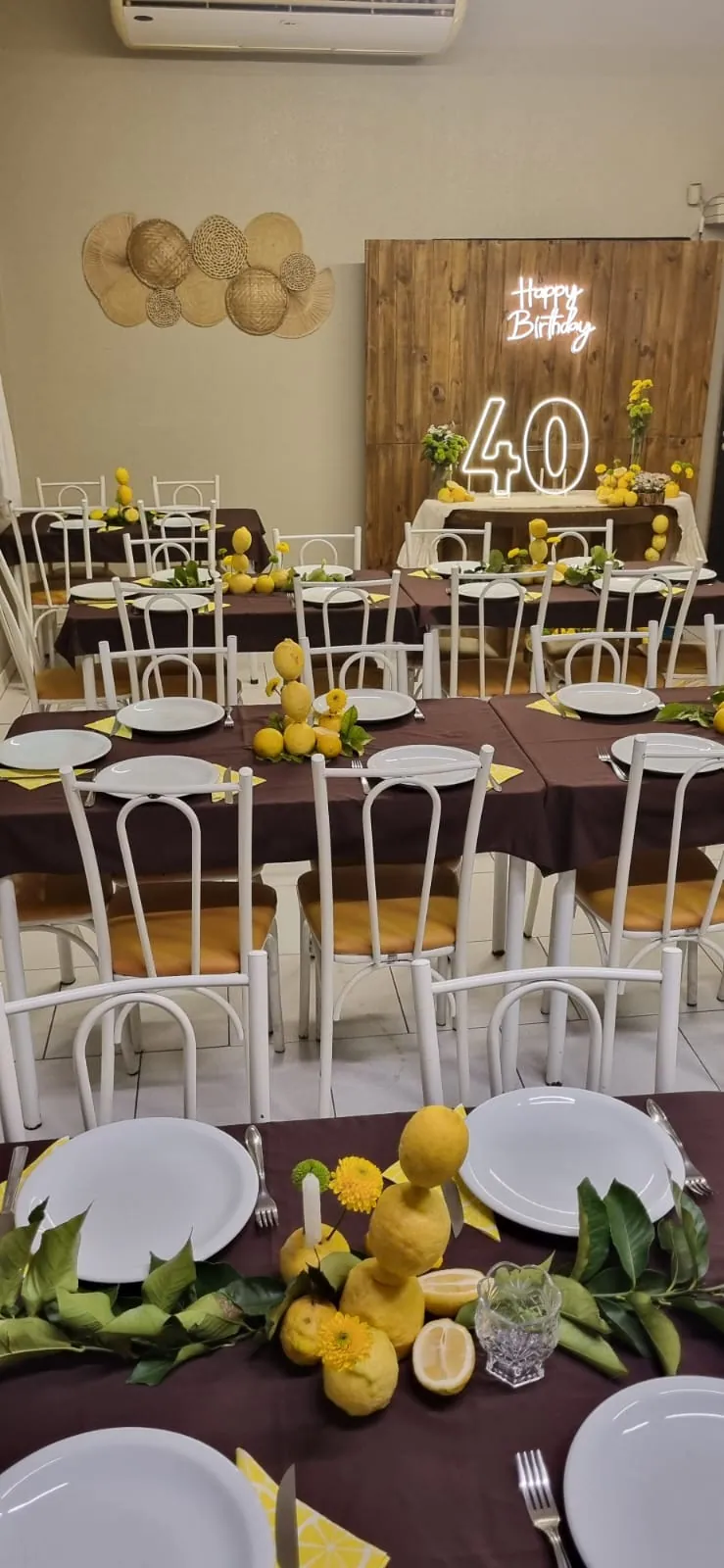 Mesas preparadas para uma celebração no Bangu com flores amarelas e decoração de aniversário